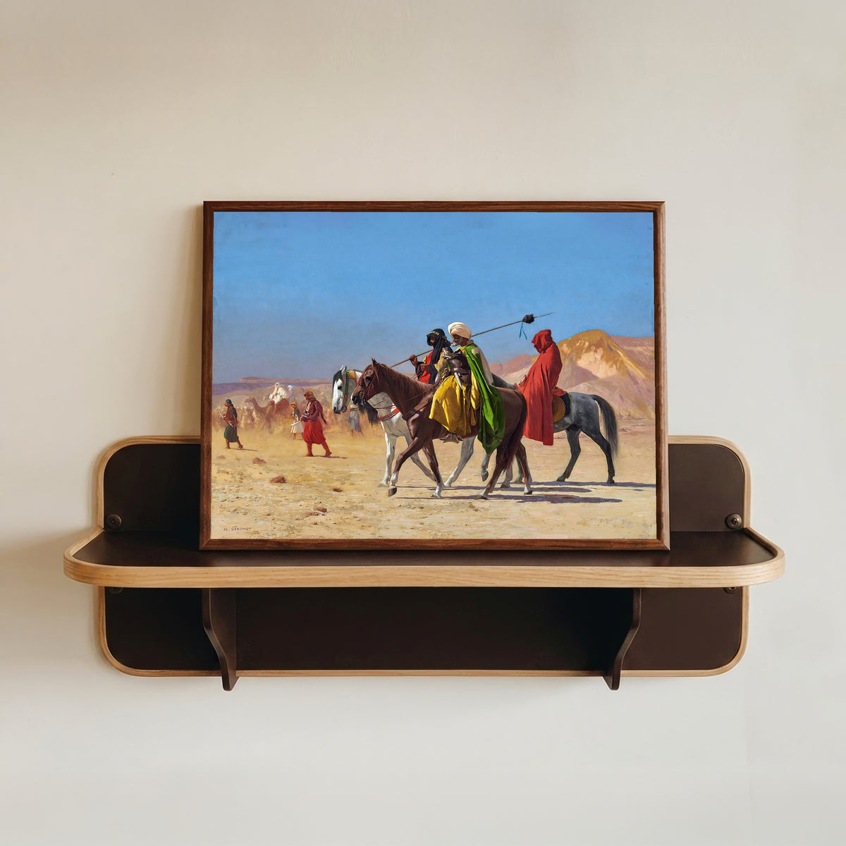 Framed art print of Riders Crossing the Desert by Jean-Léon Gérôme, in a dark wood frame resting on a wall shelf