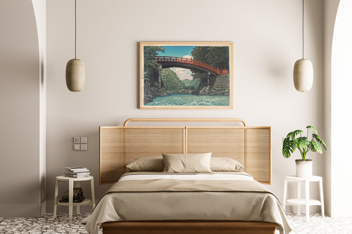 Framed art print of Sacred Bridge, Nikko by Kawase Hasui, above a cane-headboard bed