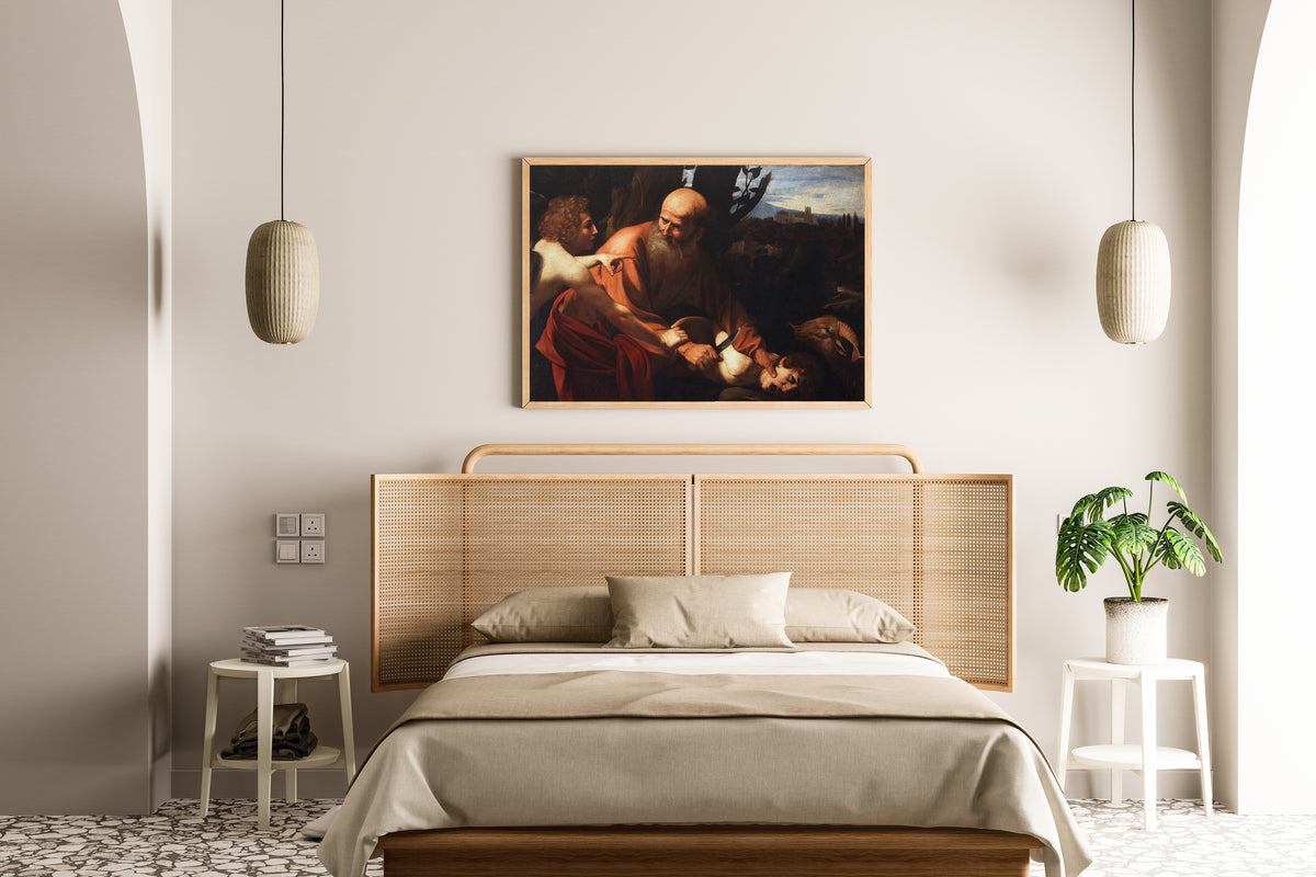 Framed art print of Sacrifice of Isaac by Caravaggio, above a cane-headboard bed