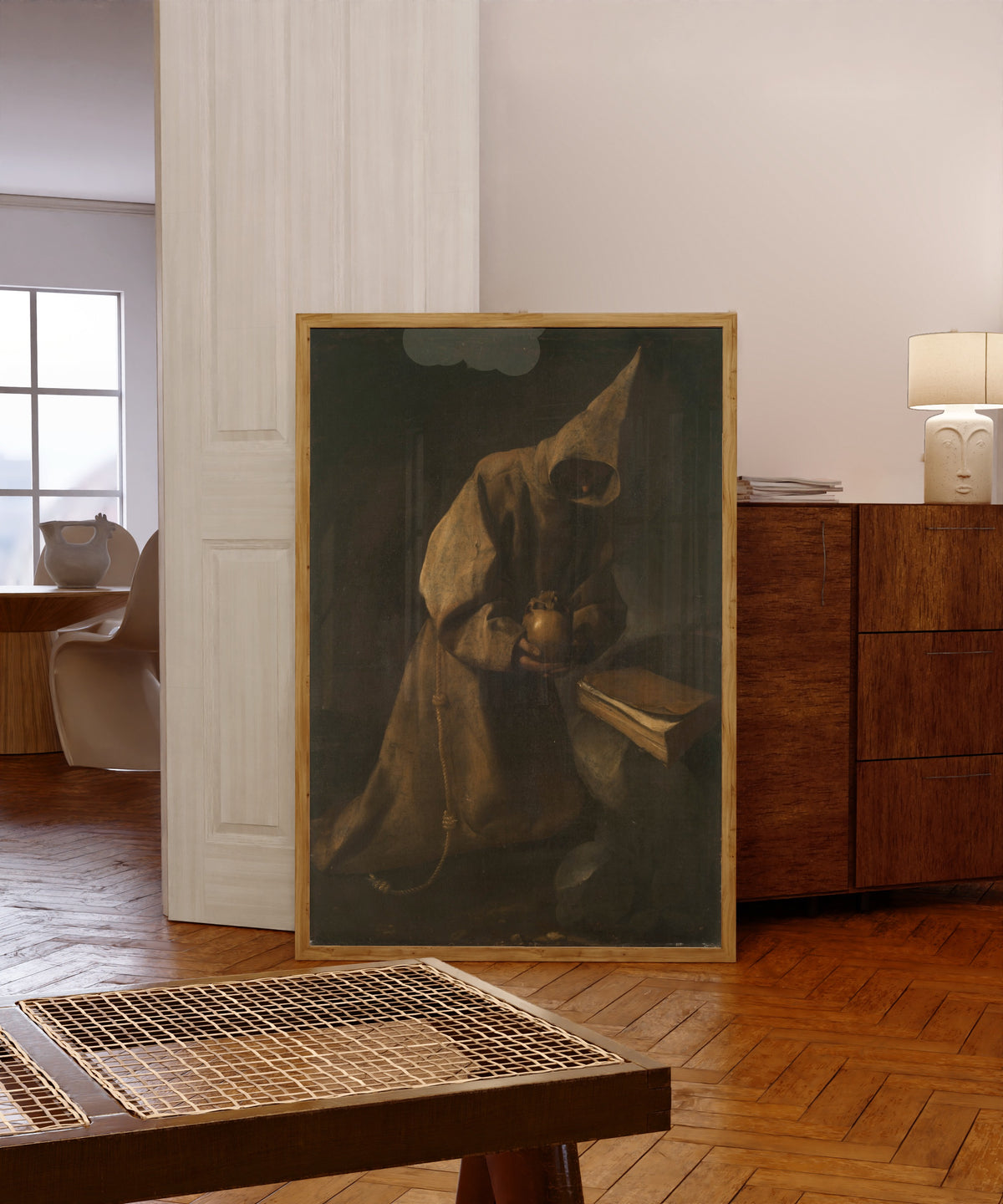 Framed art print of Saint Francis in Meditation by Francisco de Zurbarán, in a light wood frame leaning in a warm room with a parquet floor