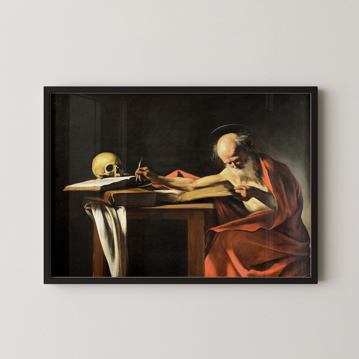 Framed art print of Saint Jerome Writing by Caravaggio, in a black frame on a pale wall
