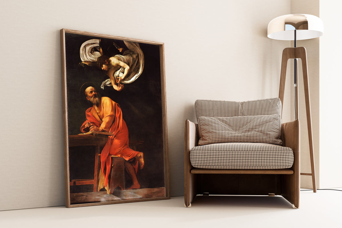 Framed art print of Saint Matthew and the angel by Caravaggio, leaning against a wall beside an armchair and a floor lamp