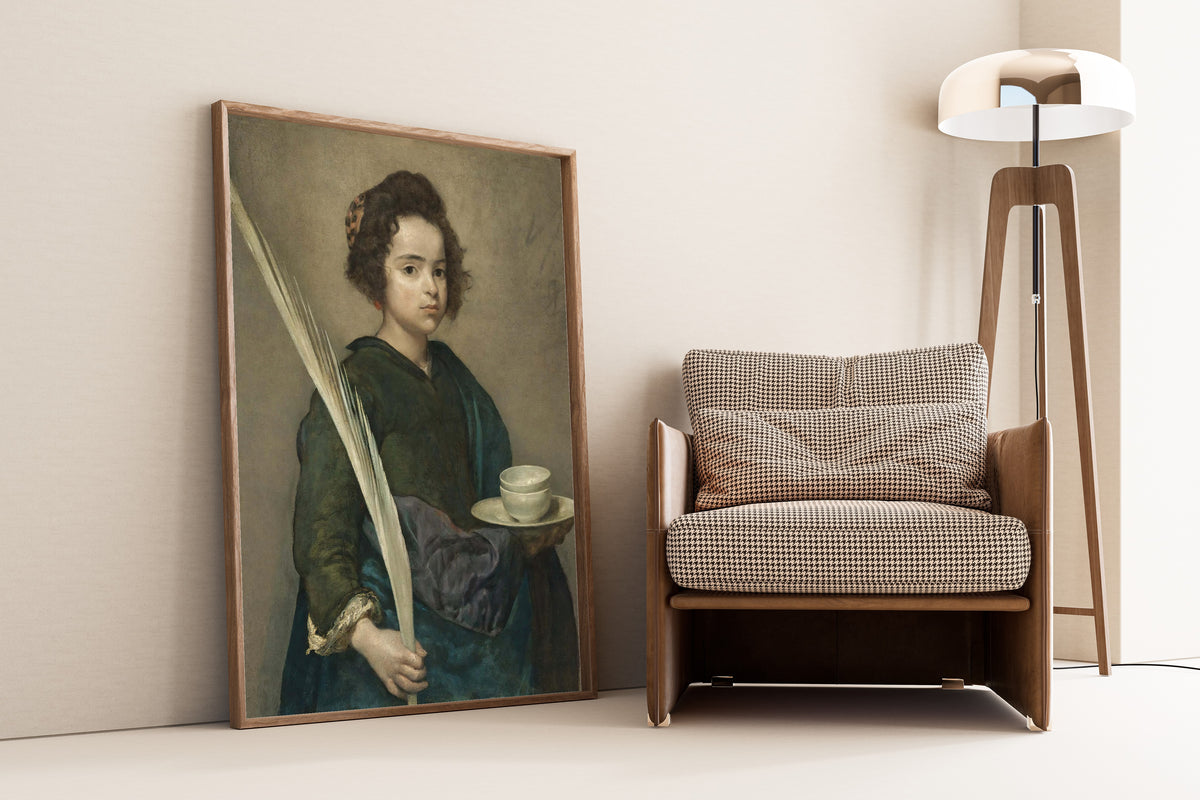 Framed art print of Saint Rufina by Diego Velázquez, leaning against a wall beside an armchair and a floor lamp