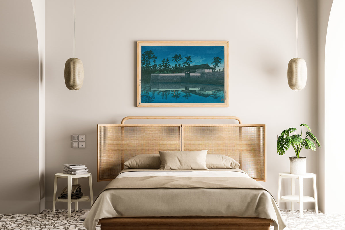 Framed art print of Sakurada Gate by Kawase Hasui, above a cane-headboard bed