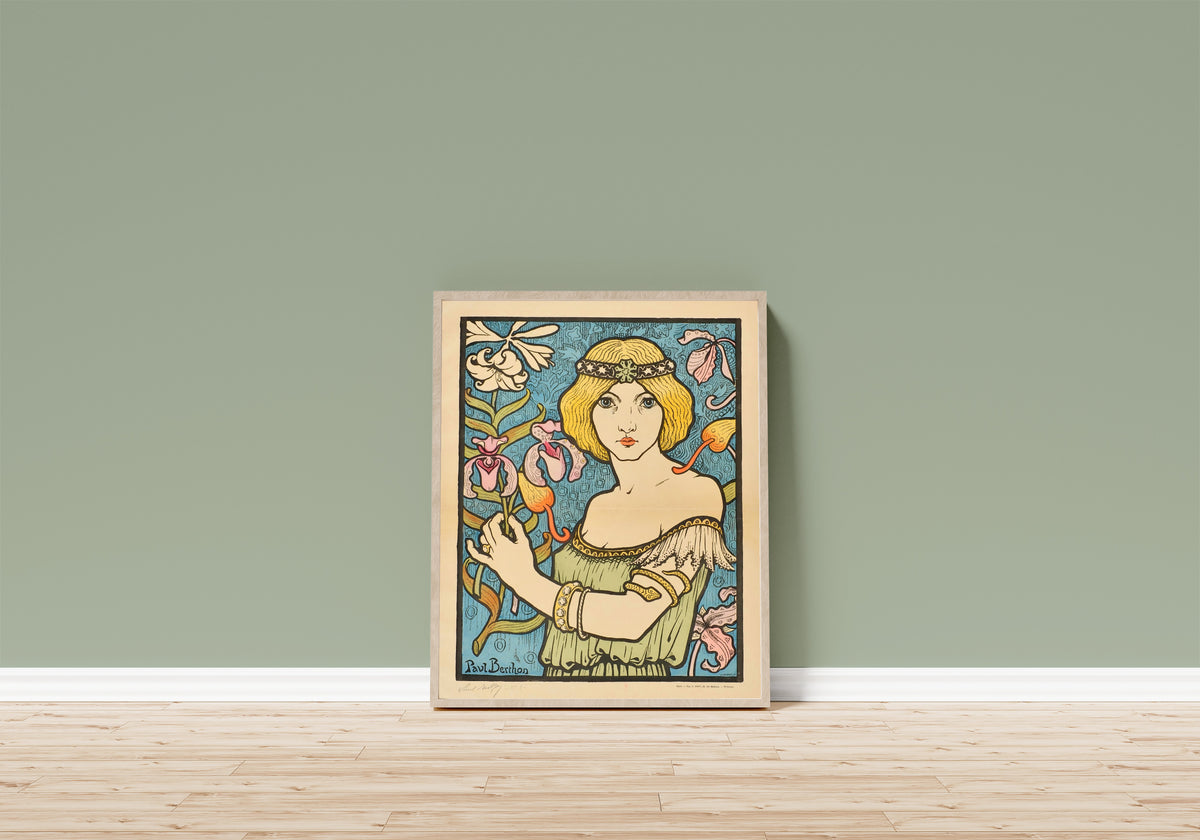 Framed art print of Salon des Cent: 17e Exposition (unlettered state) by Paul Berthon, in a light wood frame leaning on a sage green wall above a wooden floor