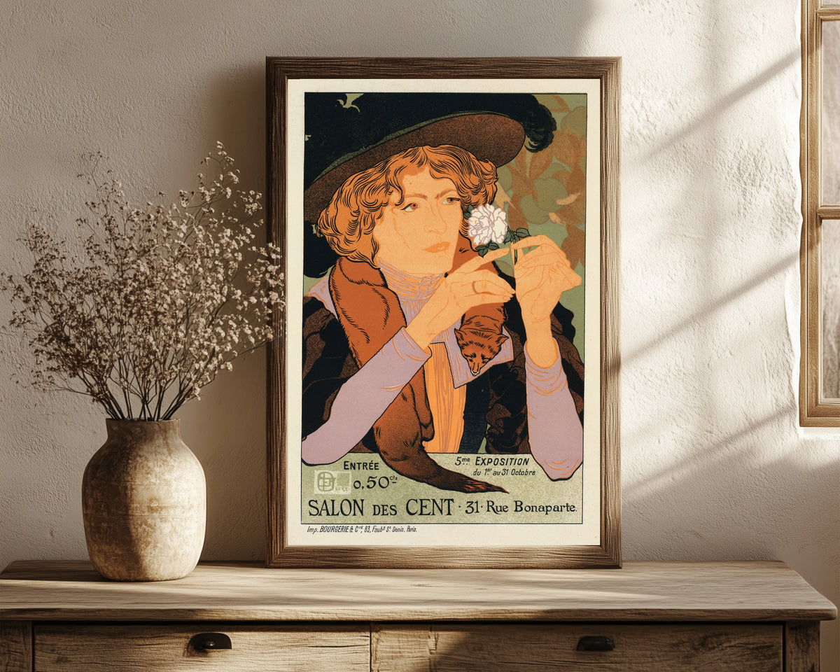 Framed art print of Salon des Cent: 5e Exposition d'Art by Georges de Feure, in a dark wood frame leaning on a rustic console beside dried flowers