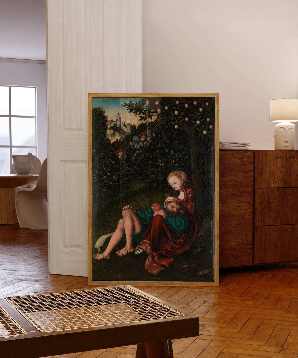 Framed art print of Samson and Delilah by Lucas Cranach the Elder, in a light wood frame leaning in a warm room with a parquet floor