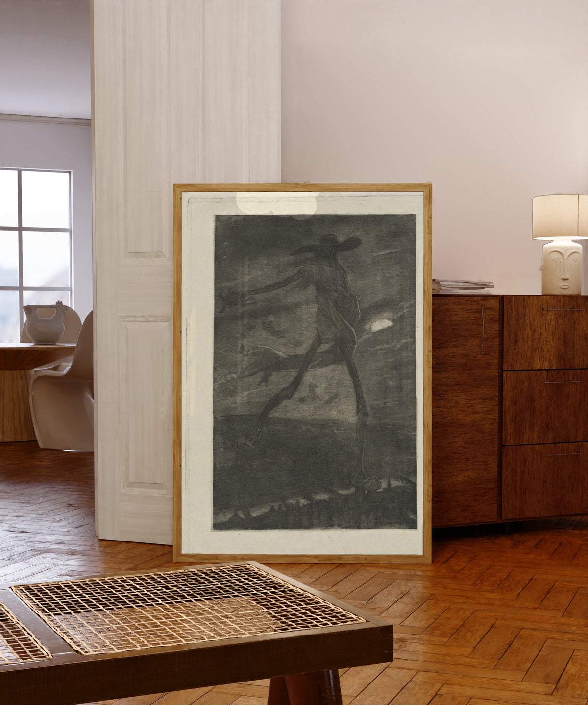 Framed art print of Satan Sowing Tares (Satan semant l'ivraie) by Félicien Rops, in a light wood frame leaning in a warm room with a parquet floor