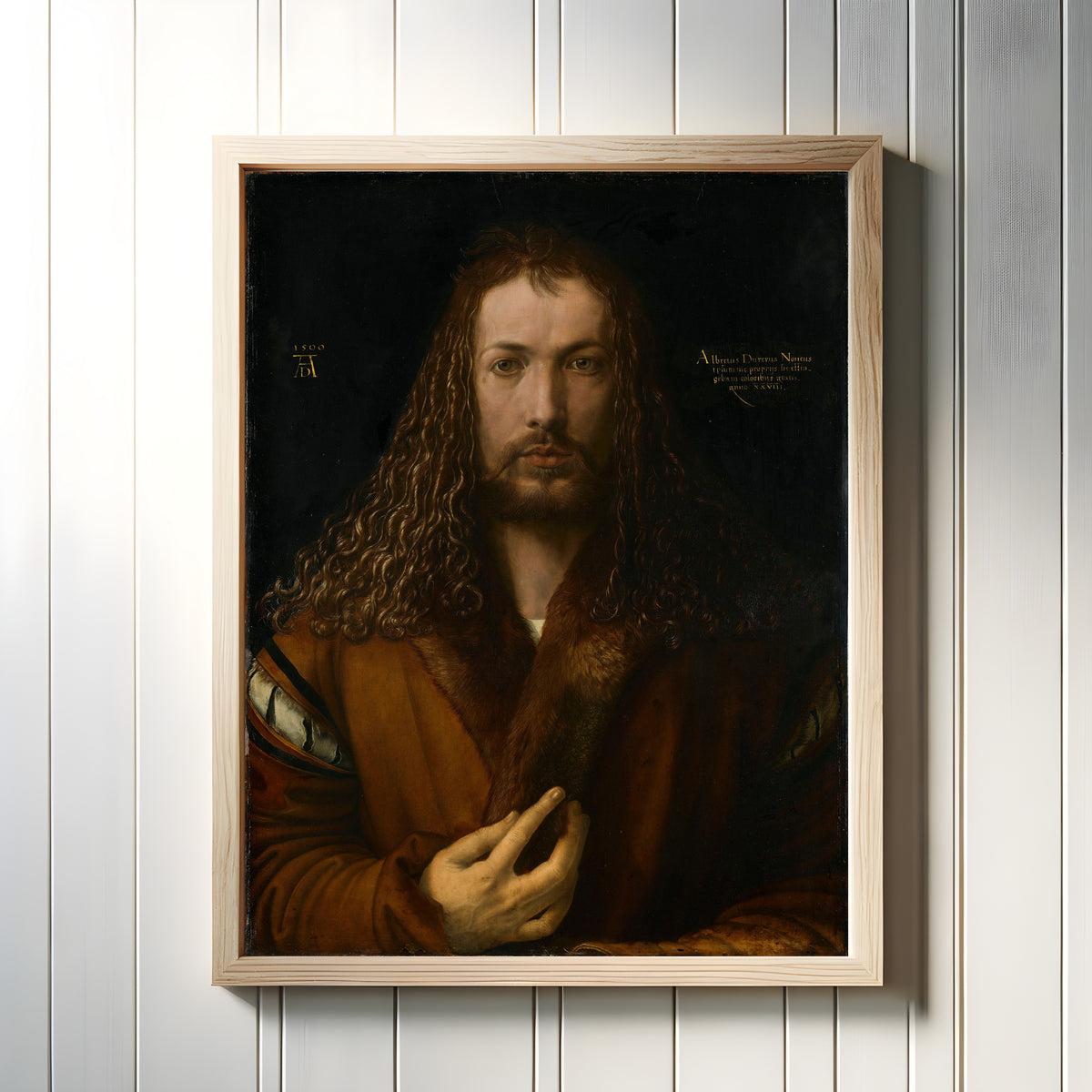Framed art print of Self-Portrait in a Fur-Trimmed Coat by Albrecht Dürer, in a light wood frame on a white panelled wall