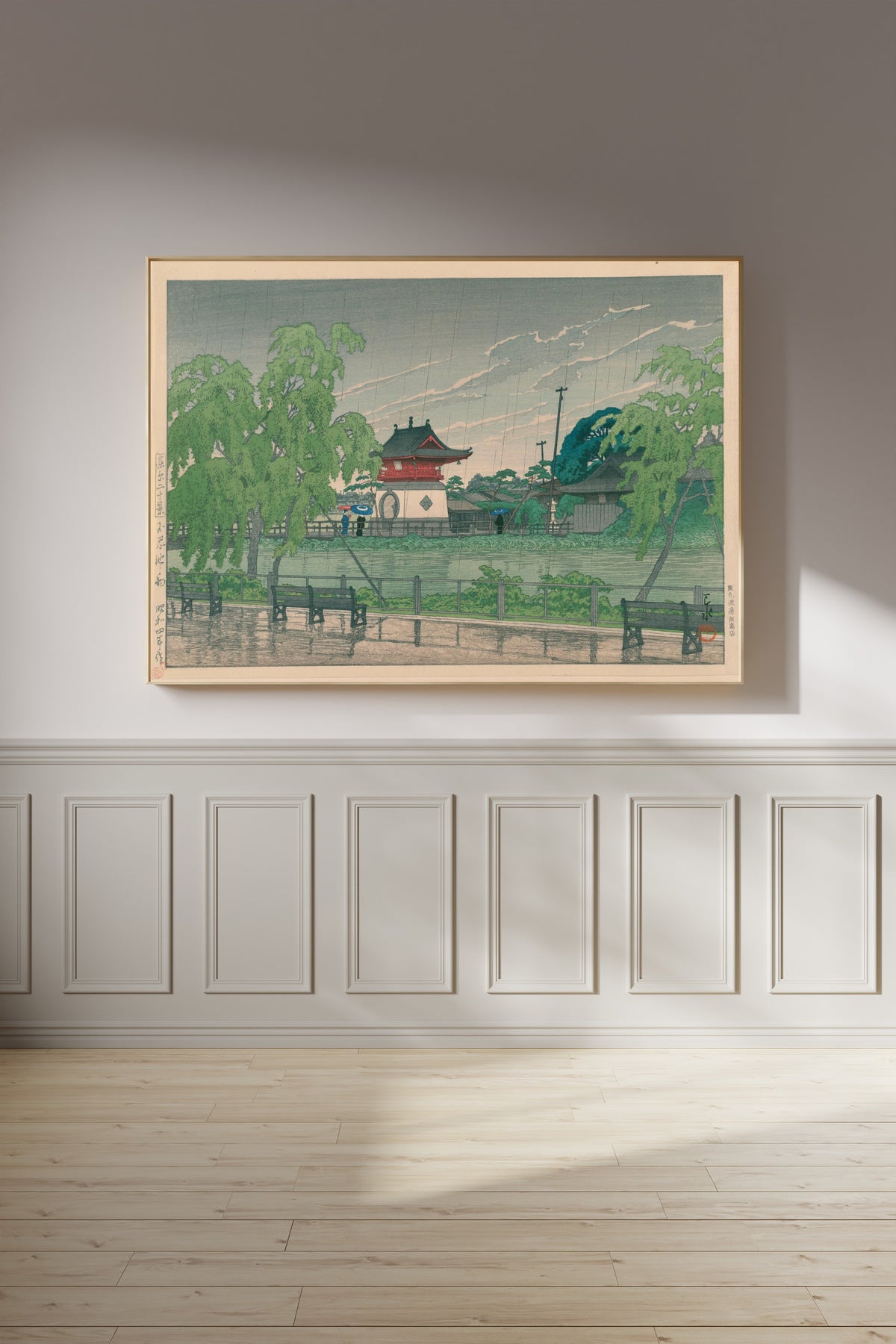 Framed art print of Shinobazu Pond in Rain by Kawase Hasui, on a panelled wall in afternoon light