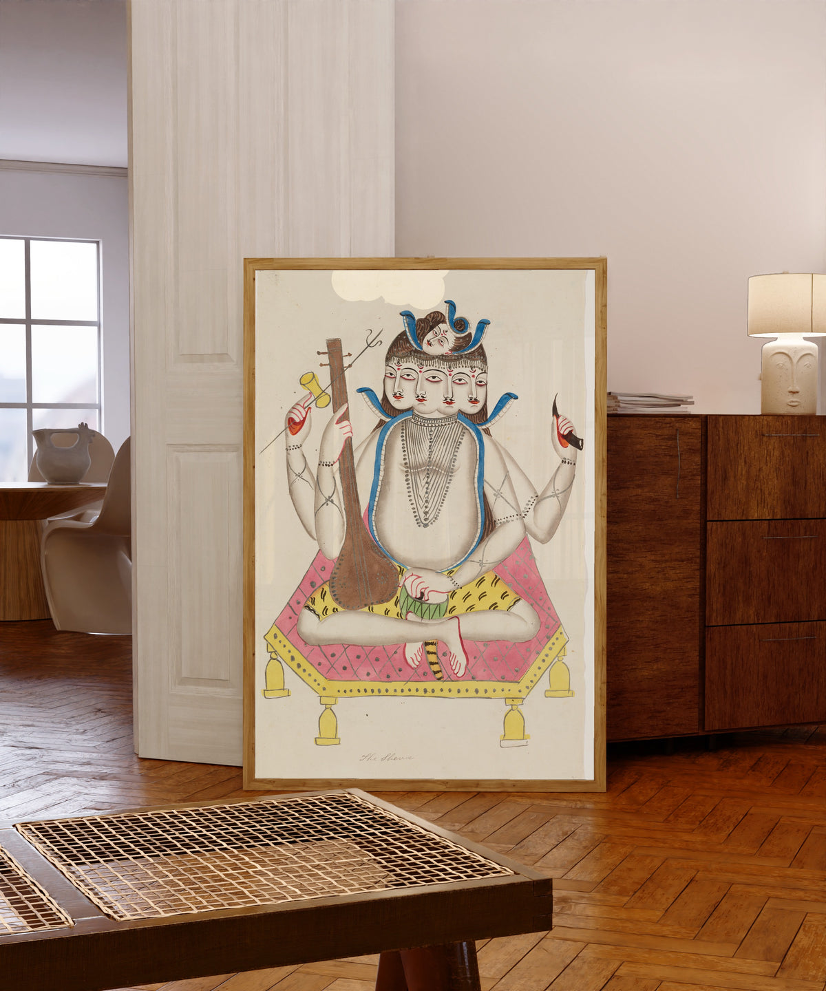 Framed art print of Shiva with Five Faces by Kalighat painter, in a light wood frame leaning in a warm room with a parquet floor