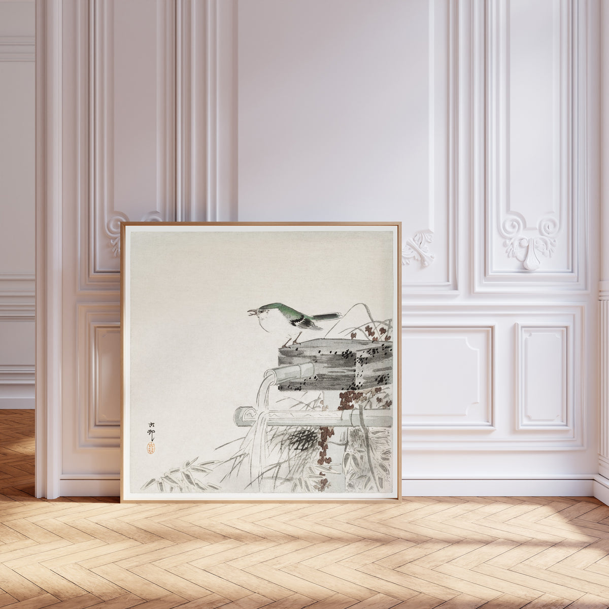 Framed art print of Siberian Blue Robin at a Bamboo Water Spout by Ohara Koson, leaning against pale pink panelling on a herringbone floor