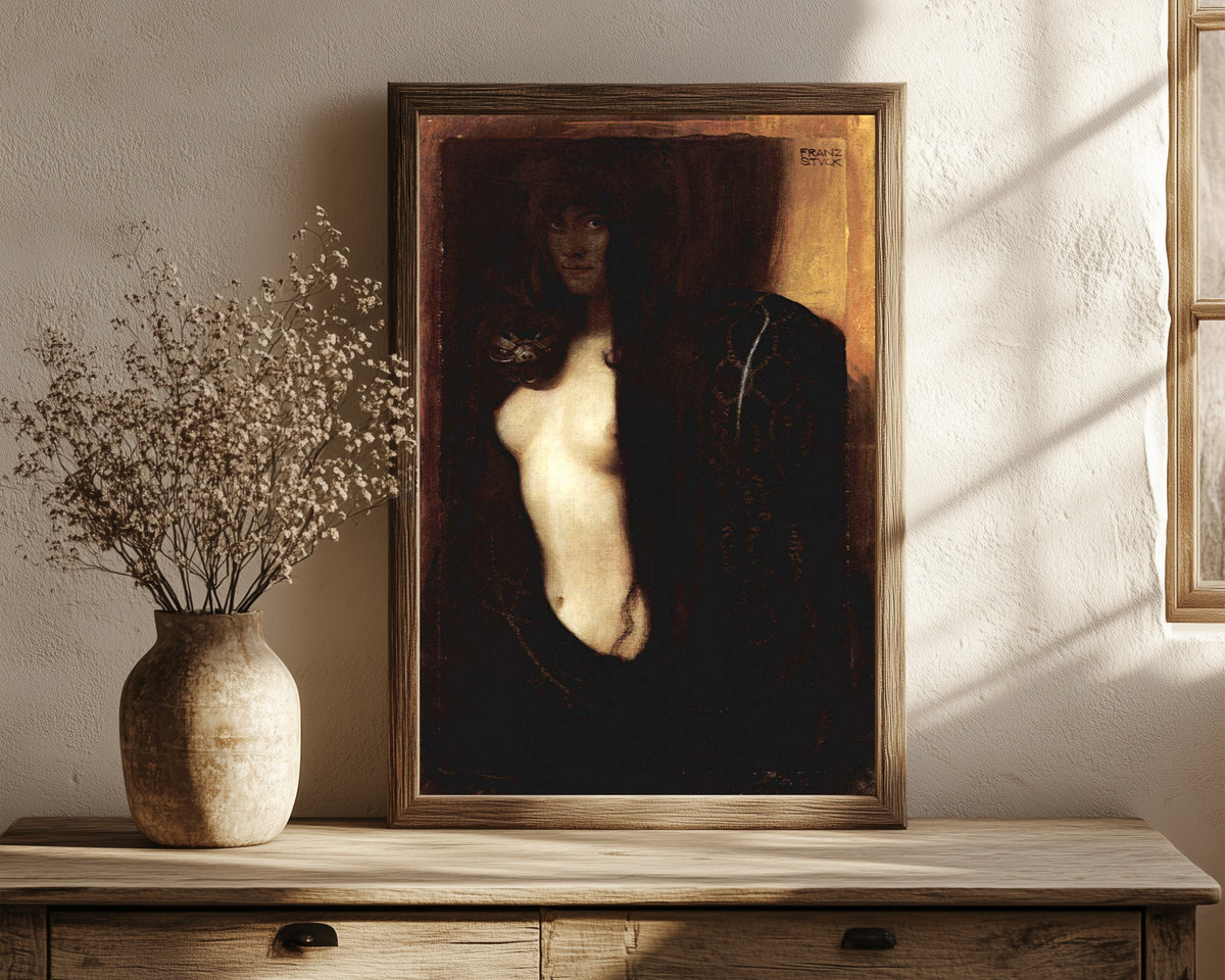 Framed art print of Sin (Die Sünde) by Franz von Stuck, in a dark wood frame leaning on a rustic console beside dried flowers