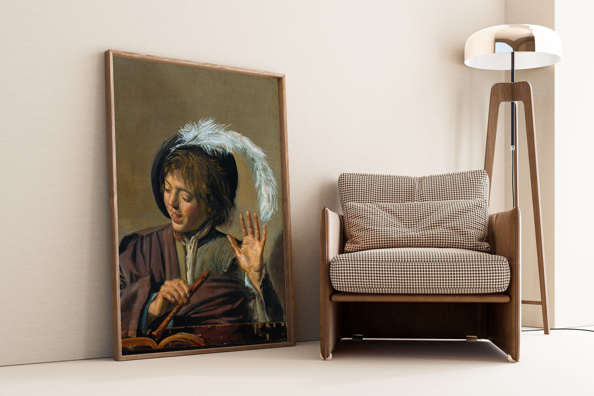 Framed art print of Singing Boy with Flute by Frans Hals, leaning against a wall beside an armchair and a floor lamp