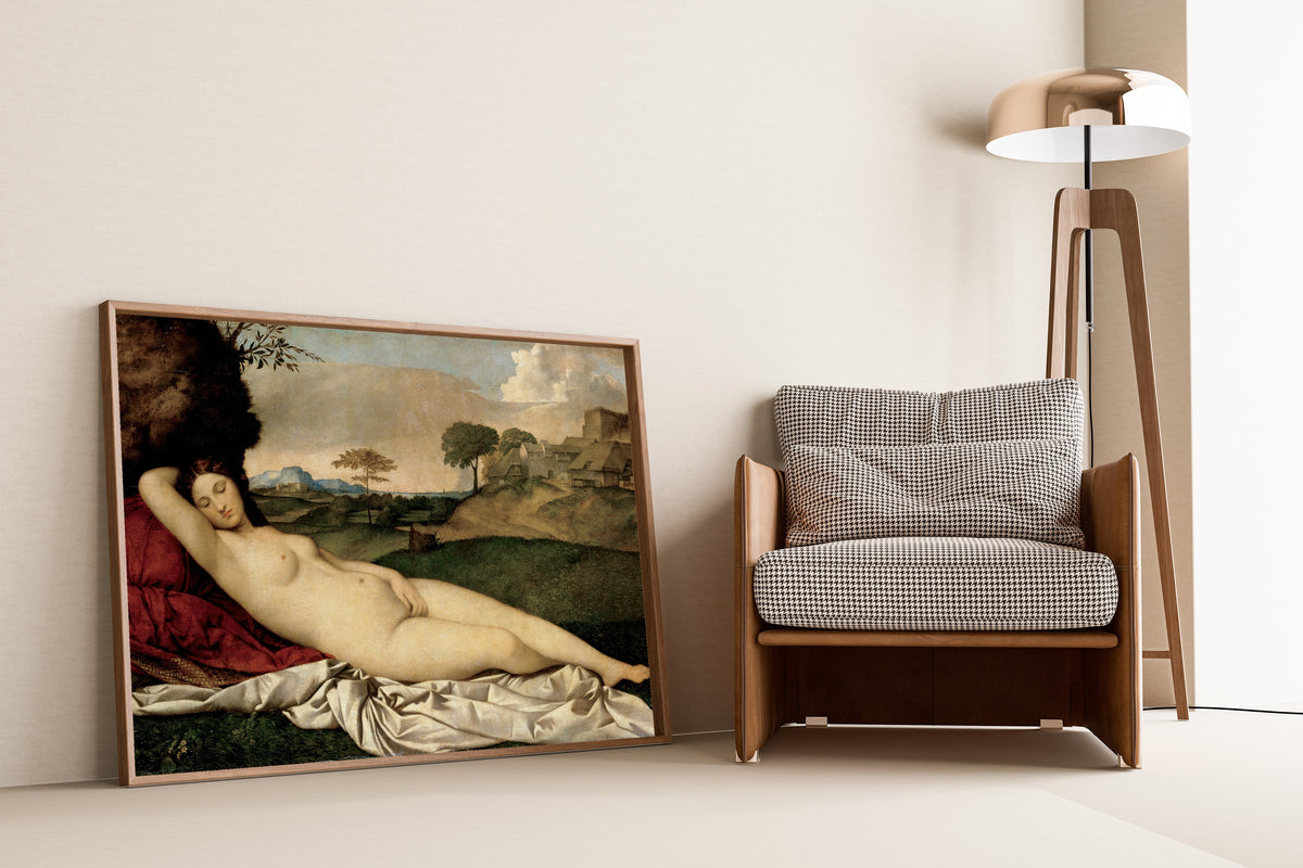 Framed art print of Sleeping Venus by Giorgione, leaning against a wall beside an armchair and a floor lamp