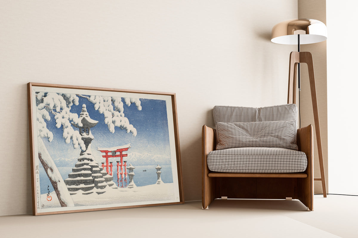 Framed art print of Snow at Itsukushima by Kawase Hasui, leaning against a wall beside an armchair and a floor lamp