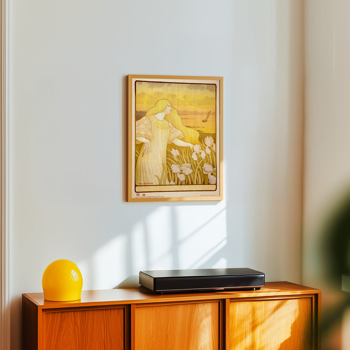 Framed art print of Société des Amis des Arts de la Manche (unlettered state) by Paul Berthon, in a light wood frame on a white wall above an orange sideboard