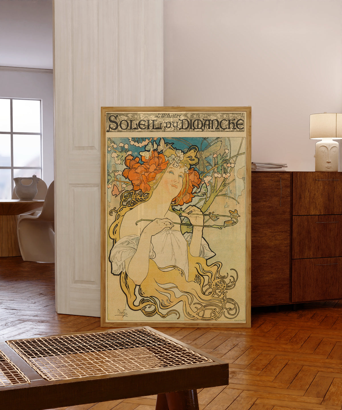 Framed art print of Soleil du Dimanche by Alphonse Mucha, in a light wood frame leaning in a warm room with a parquet floor