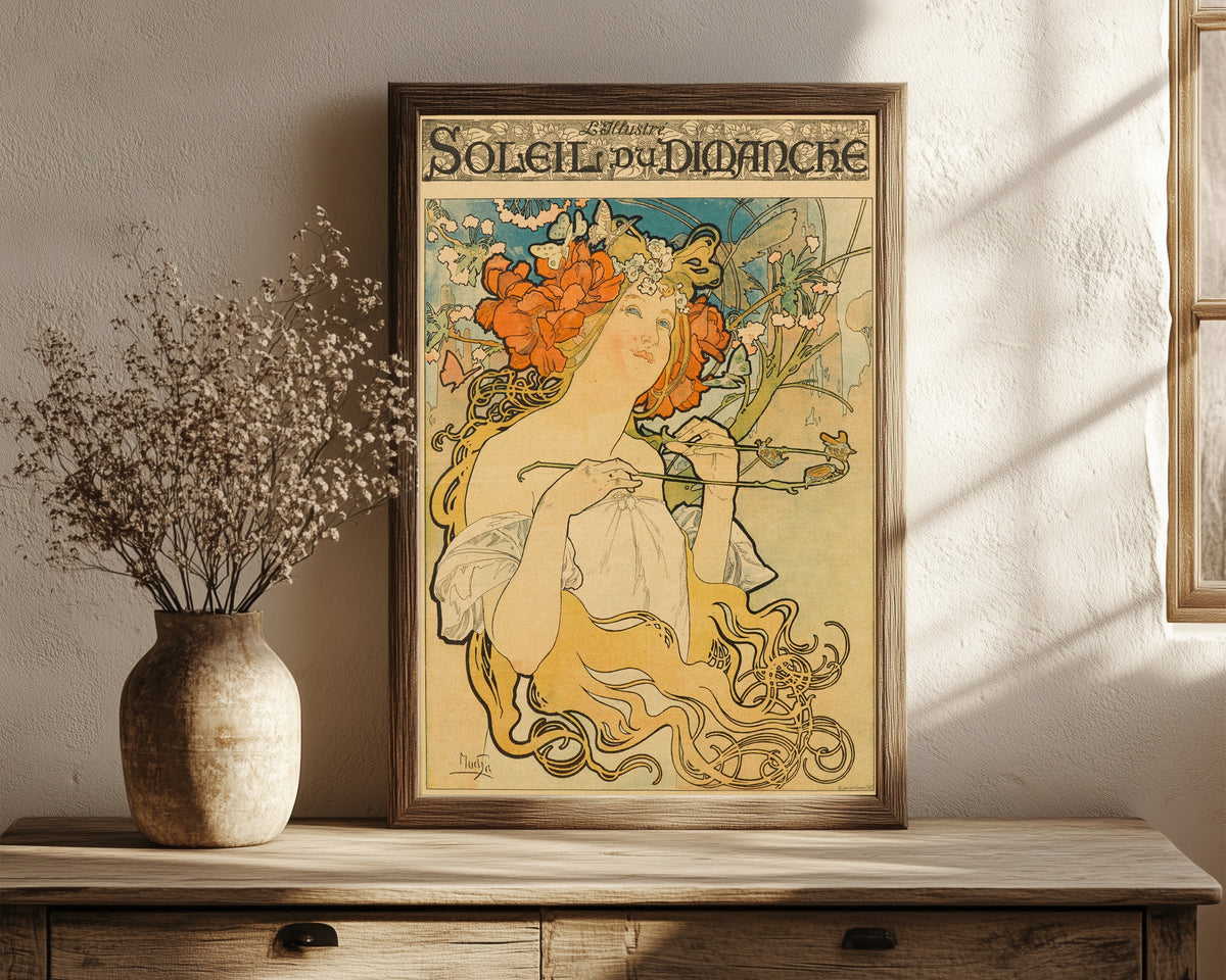 Framed art print of Soleil du Dimanche by Alphonse Mucha, in a dark wood frame leaning on a rustic console beside dried flowers