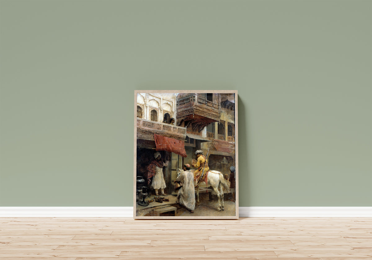 Framed art print of Street Scene in India by Edwin Lord Weeks, in a light wood frame leaning on a sage green wall above a wooden floor