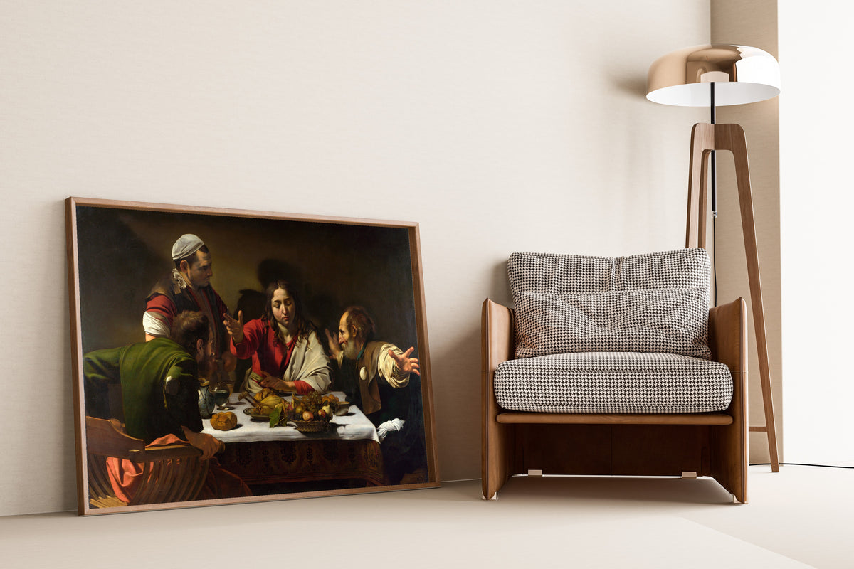 Framed art print of Supper at Emmaus by Caravaggio, leaning against a wall beside an armchair and a floor lamp