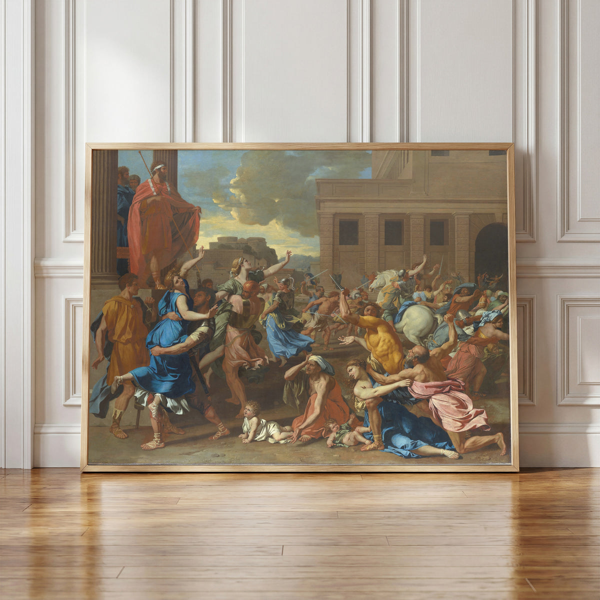 Framed art print of The Abduction of the Sabine Women by Nicolas Poussin, in a light wood frame leaning against a panelled white wall