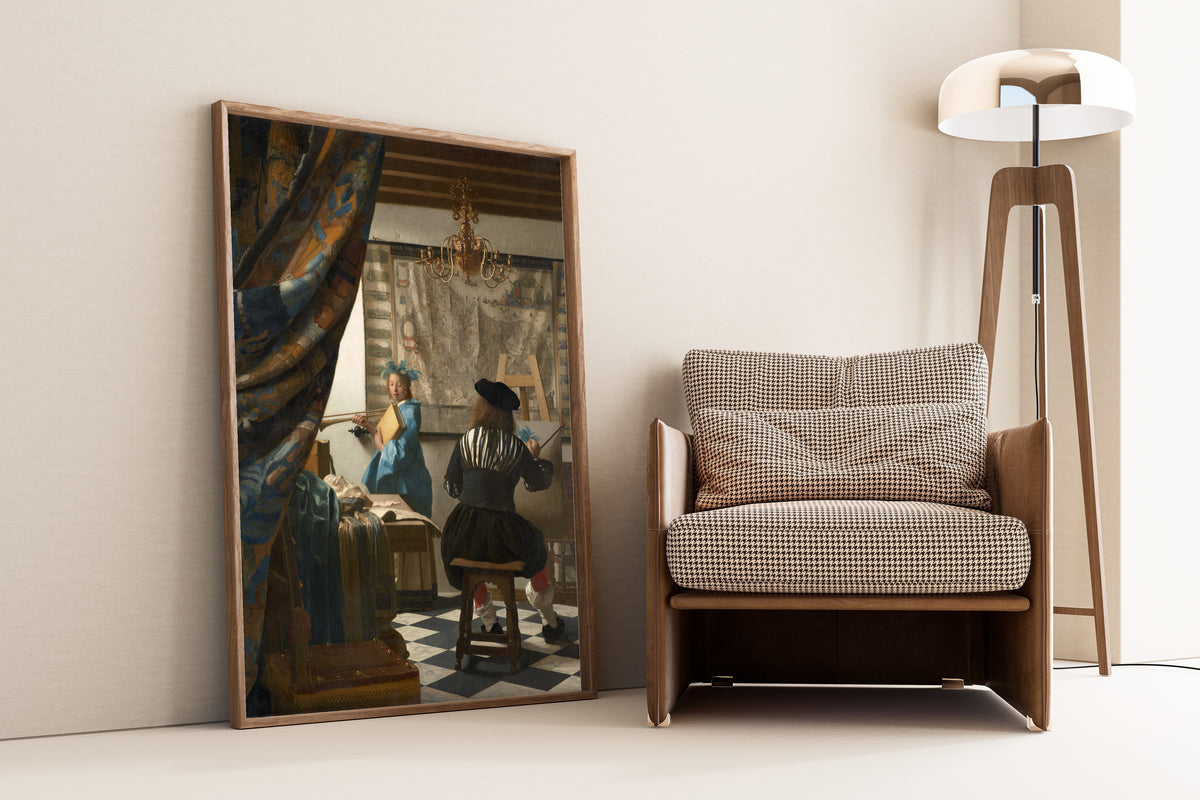 Framed art print of The Art of Painting by Johannes Vermeer, leaning against a wall beside an armchair and a floor lamp