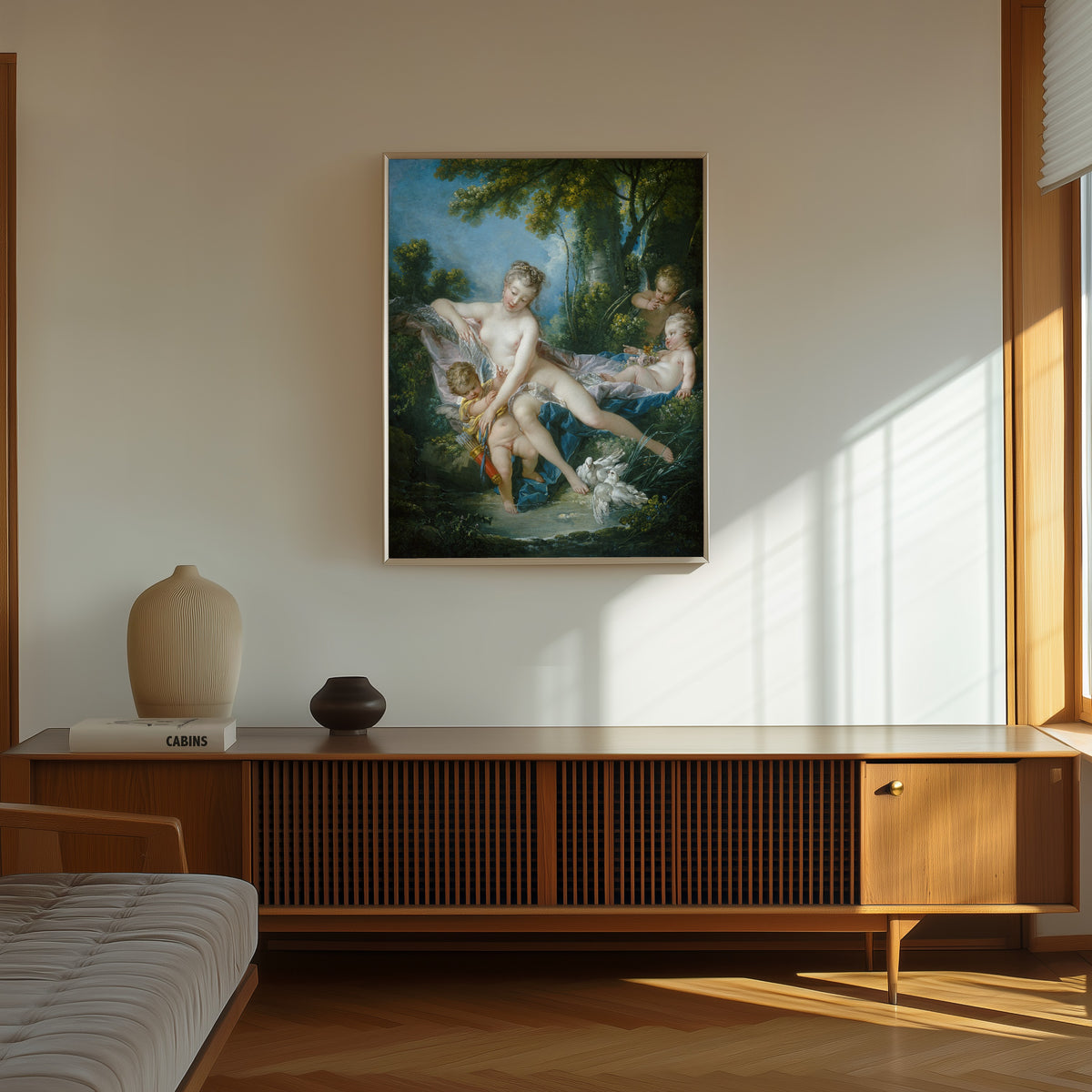 Framed art print of The Bath of Venus by François Boucher, in a thin light frame on a sunlit wall above a wooden sideboard
