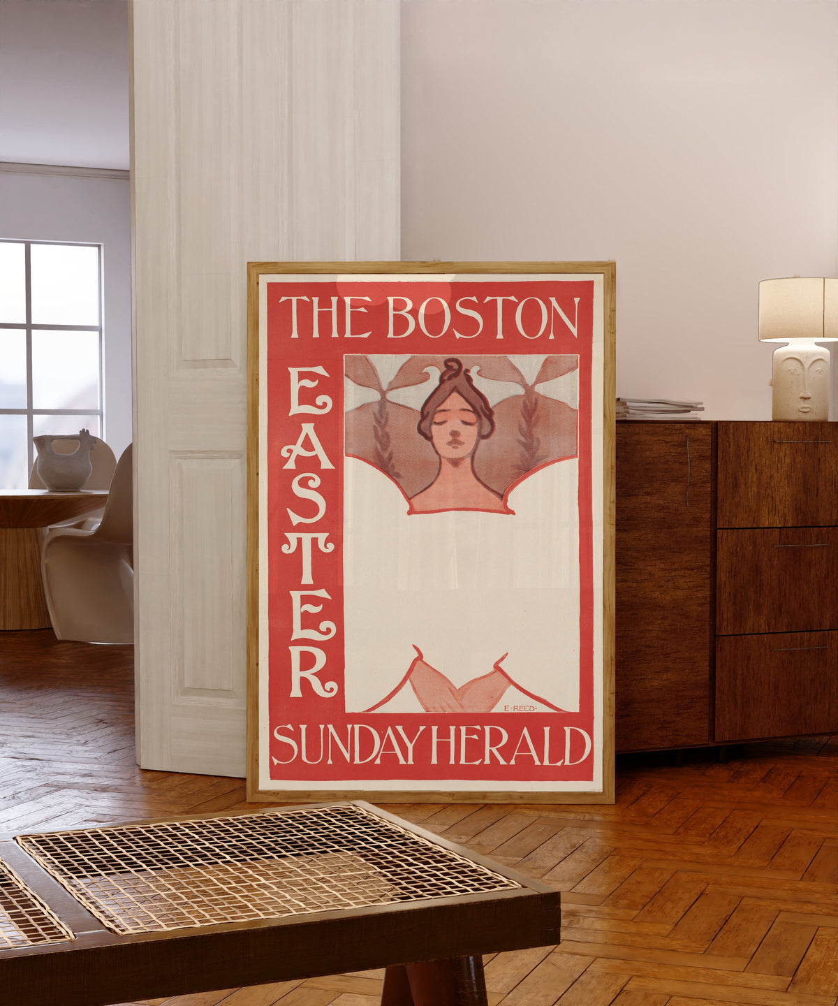 Framed art print of The Boston Sunday Herald, Easter by Ethel Reed, in a light wood frame leaning in a warm room with a parquet floor