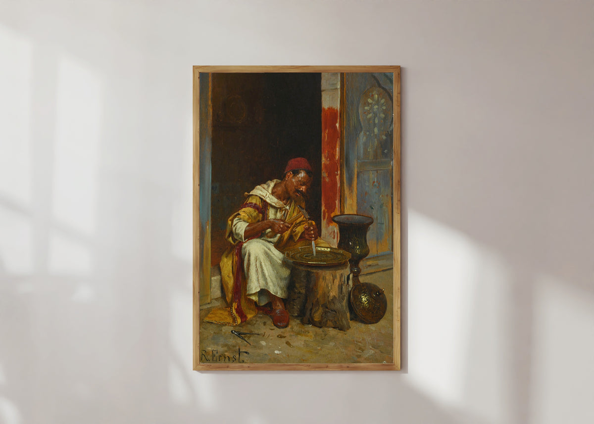 Framed art print of The Brass Worker by Rudolf Ernst, in a light wood frame on a sunlit white wall