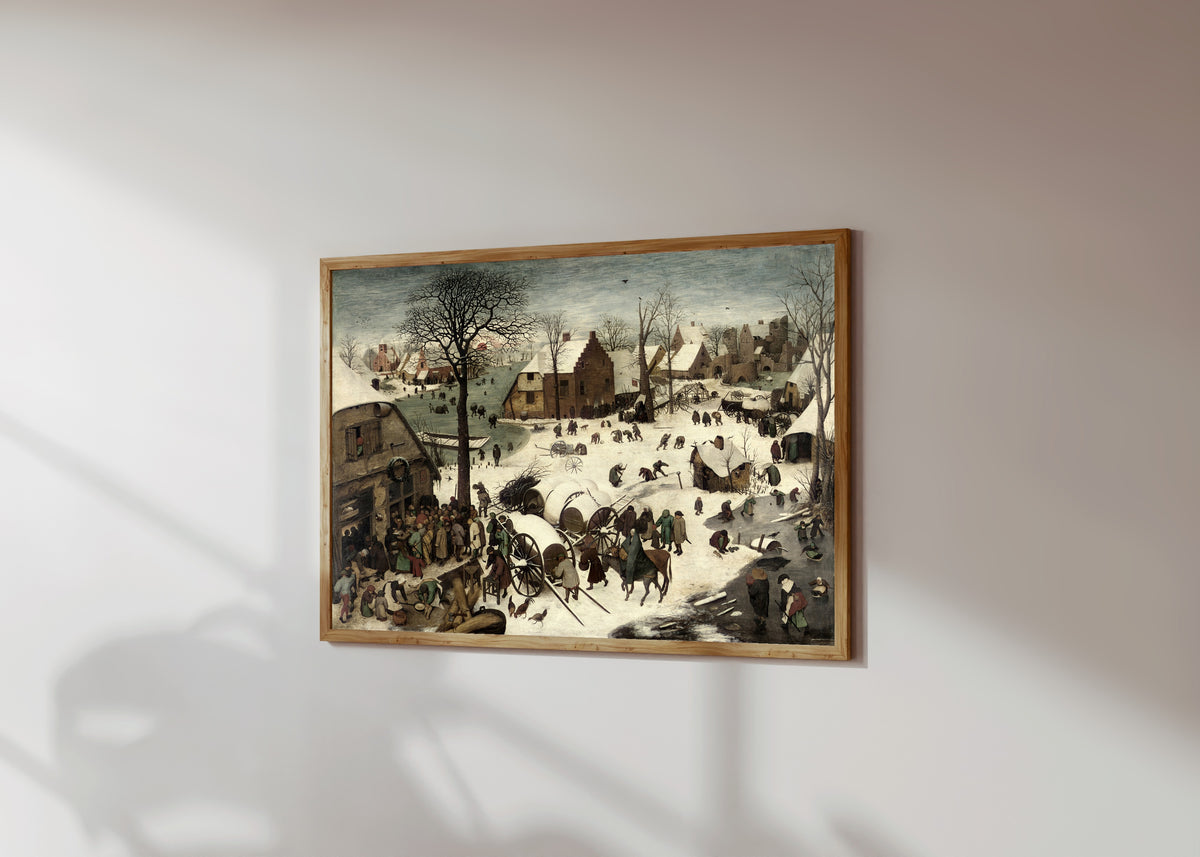 Framed art print of The Census at Bethlehem by Pieter Bruegel the Elder, in a light wood frame on a sunlit white wall, seen at a slight angle