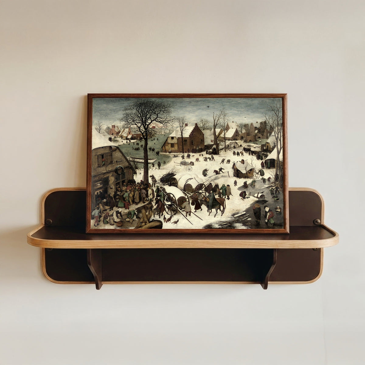 Framed art print of The Census at Bethlehem by Pieter Bruegel the Elder, in a dark wood frame resting on a wall shelf