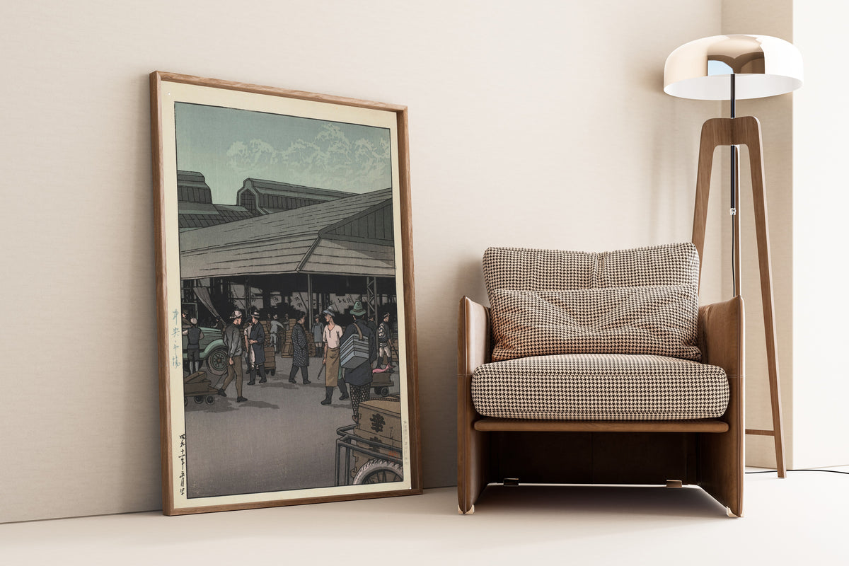 Framed art print of The Central Market by Kawase Hasui, leaning against a wall beside an armchair and a floor lamp