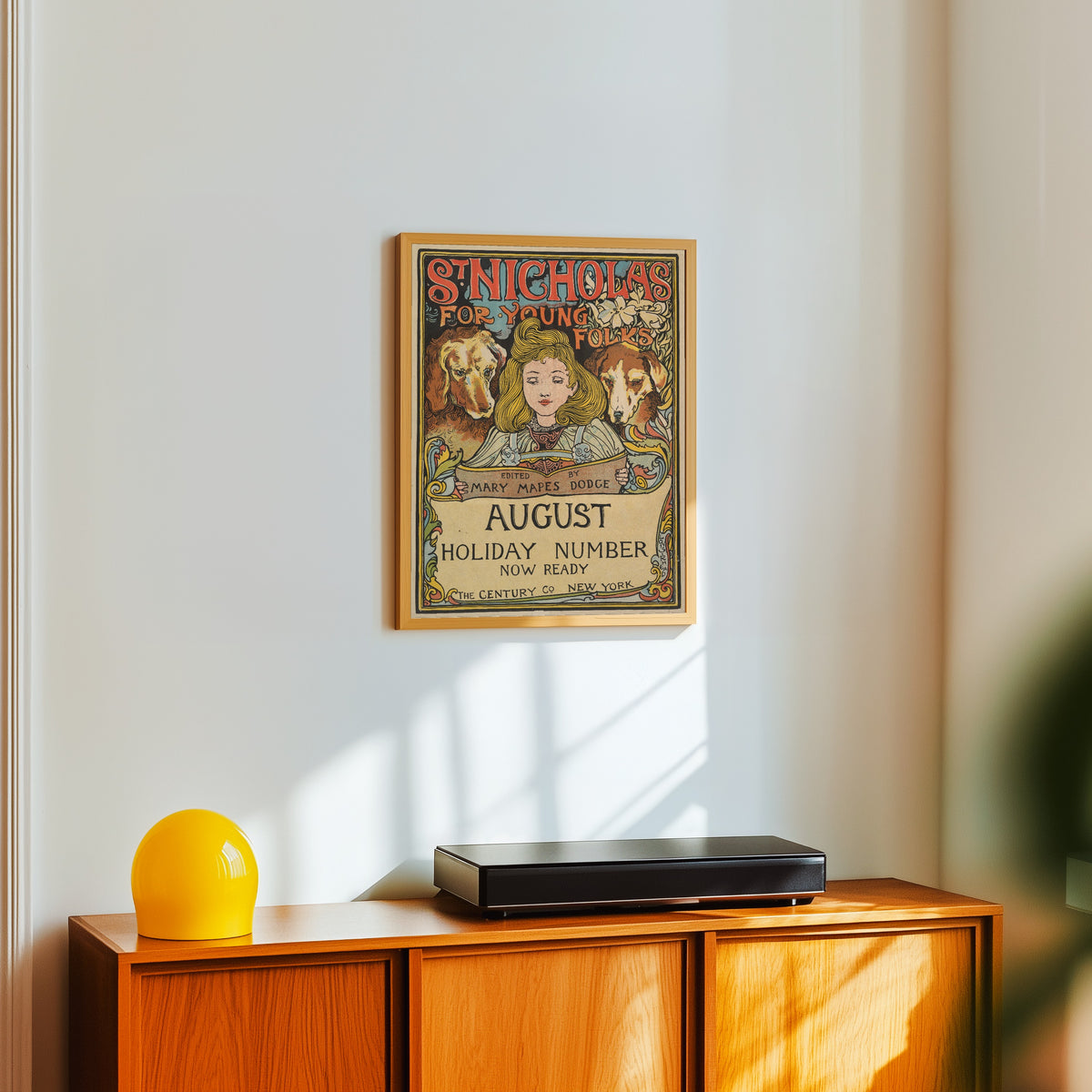 Framed art print of The Century, Holiday Number, St. Nicholas for Young Folks… by Louis Rhead, in a light wood frame on a white wall above an orange sideboard