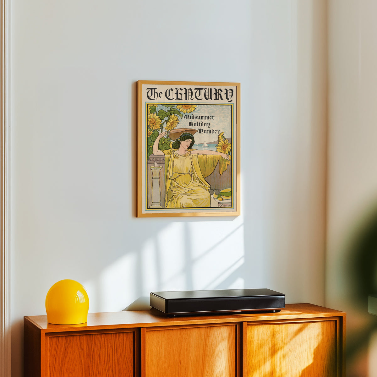 Framed art print of The Century, Midsummer Holiday Number by Louis Rhead, in a light wood frame on a white wall above an orange sideboard