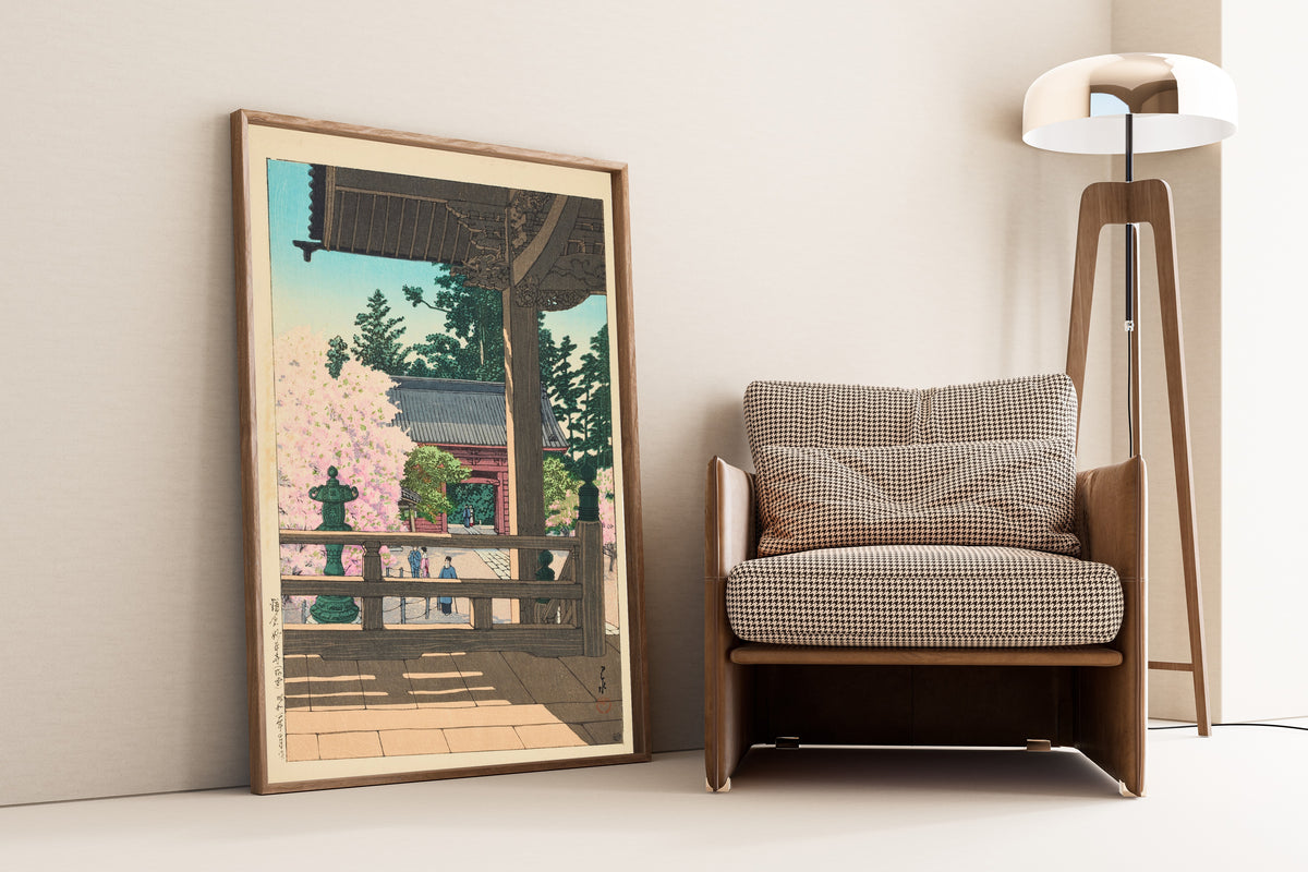 Framed art print of The Crabapple Flowers in Myohonji Temple, Kamakura by Kawase Hasui, leaning against a wall beside an armchair and a floor lamp