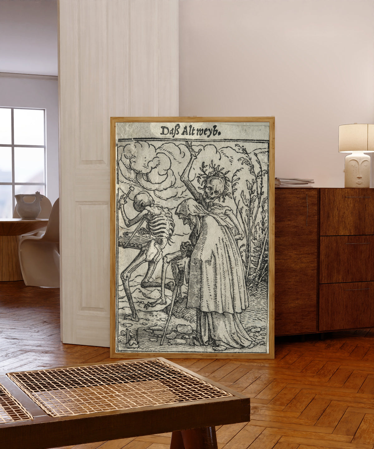 Framed art print of The Dance of Death: Daß Altweyb (The Old… by Hans Holbein the Younger, in a light wood frame leaning in a warm room with a parquet floor