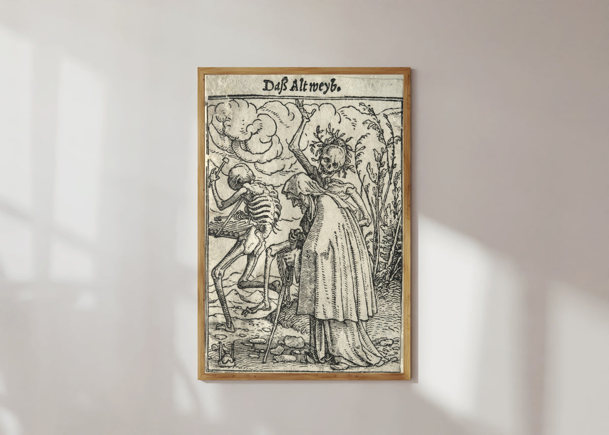 Framed art print of The Dance of Death: Daß Altweyb (The Old Woman) by Hans Holbein the Younger, in a light wood frame on a sunlit white wall