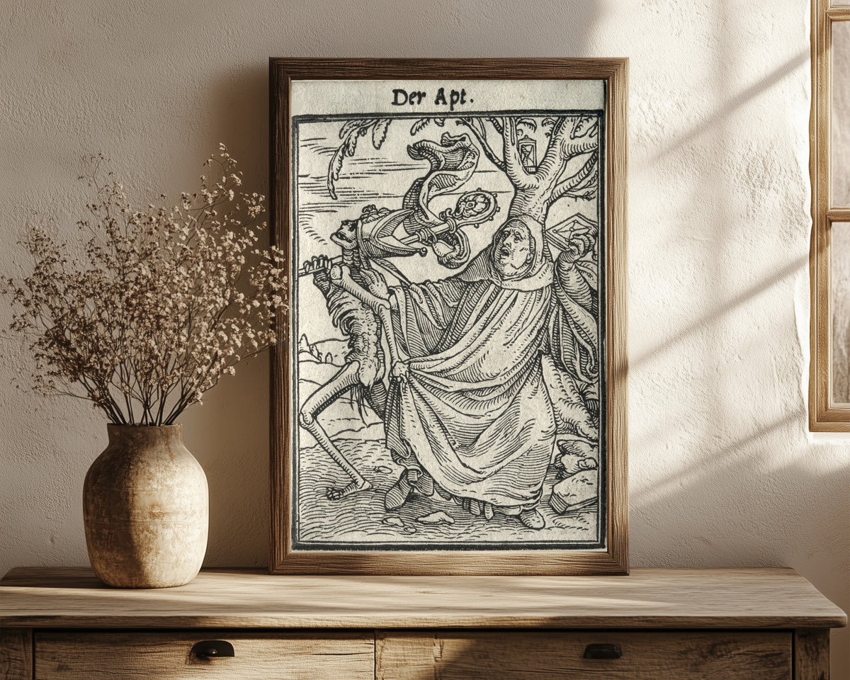 Framed art print of The Dance of Death: Der Apt (The Abbot) by Hans Holbein the Younger, in a dark wood frame leaning on a rustic console beside dried flowers