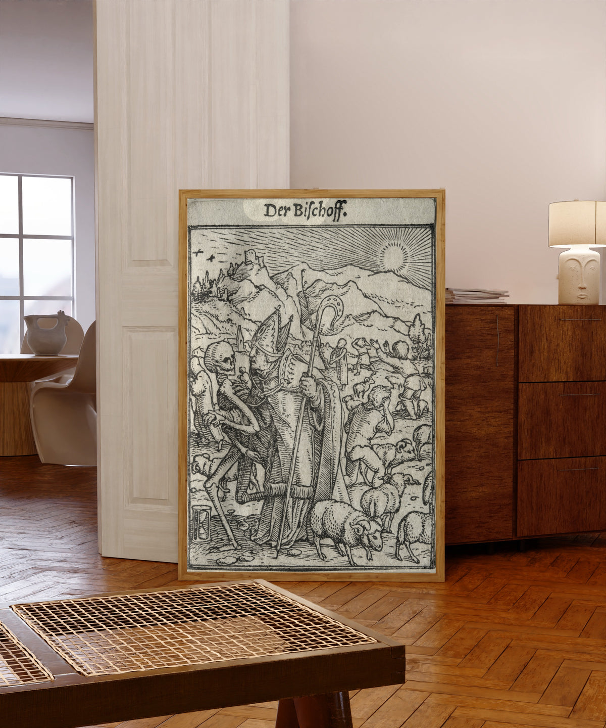 Framed art print of The Dance of Death: Der Bischoff (The Bishop) by Hans Holbein the Younger, in a light wood frame leaning in a warm room with a parquet floor