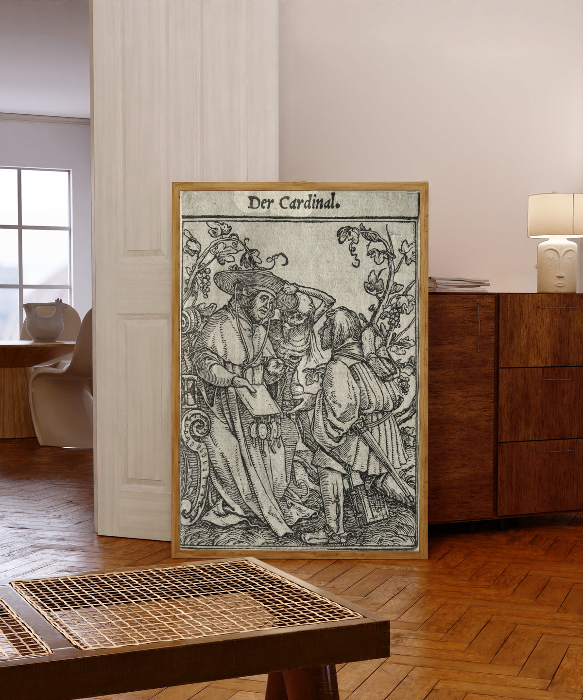 Framed art print of The Dance of Death: Der Cardinal (The… by Hans Holbein the Younger, in a light wood frame leaning in a warm room with a parquet floor