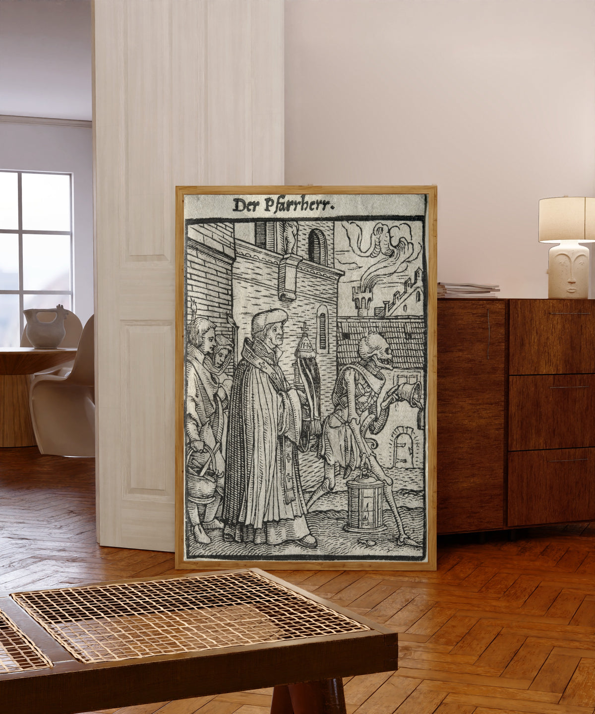 Framed art print of The Dance of Death: Der Pfarrherr (The… by Hans Holbein the Younger, in a light wood frame leaning in a warm room with a parquet floor