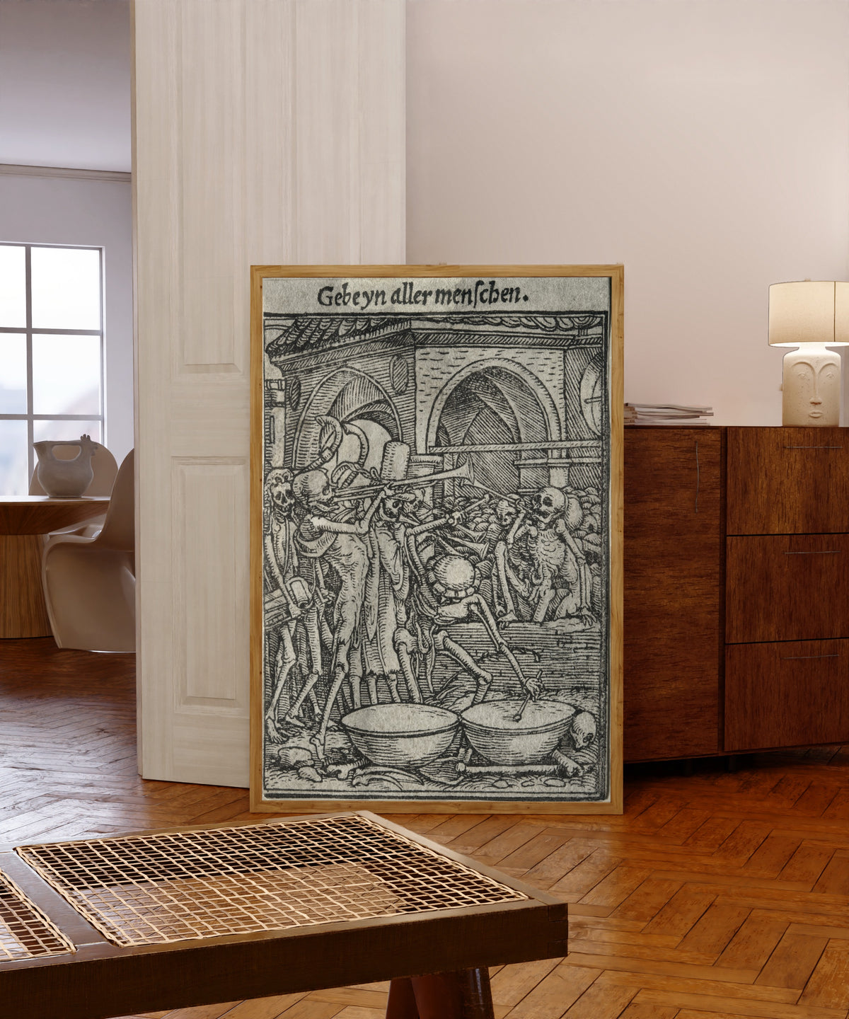Framed art print of The Dance of Death: Gebeyn aller menschen… by Hans Holbein the Younger, in a light wood frame leaning in a warm room with a parquet floor