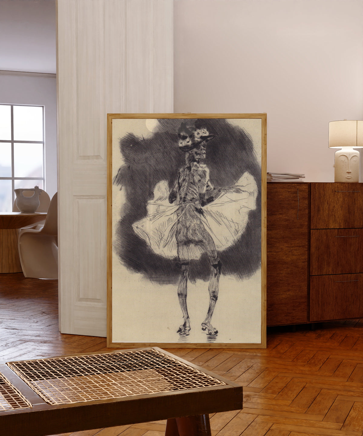 Framed art print of The Dance of Death by Félicien Rops, in a light wood frame leaning in a warm room with a parquet floor