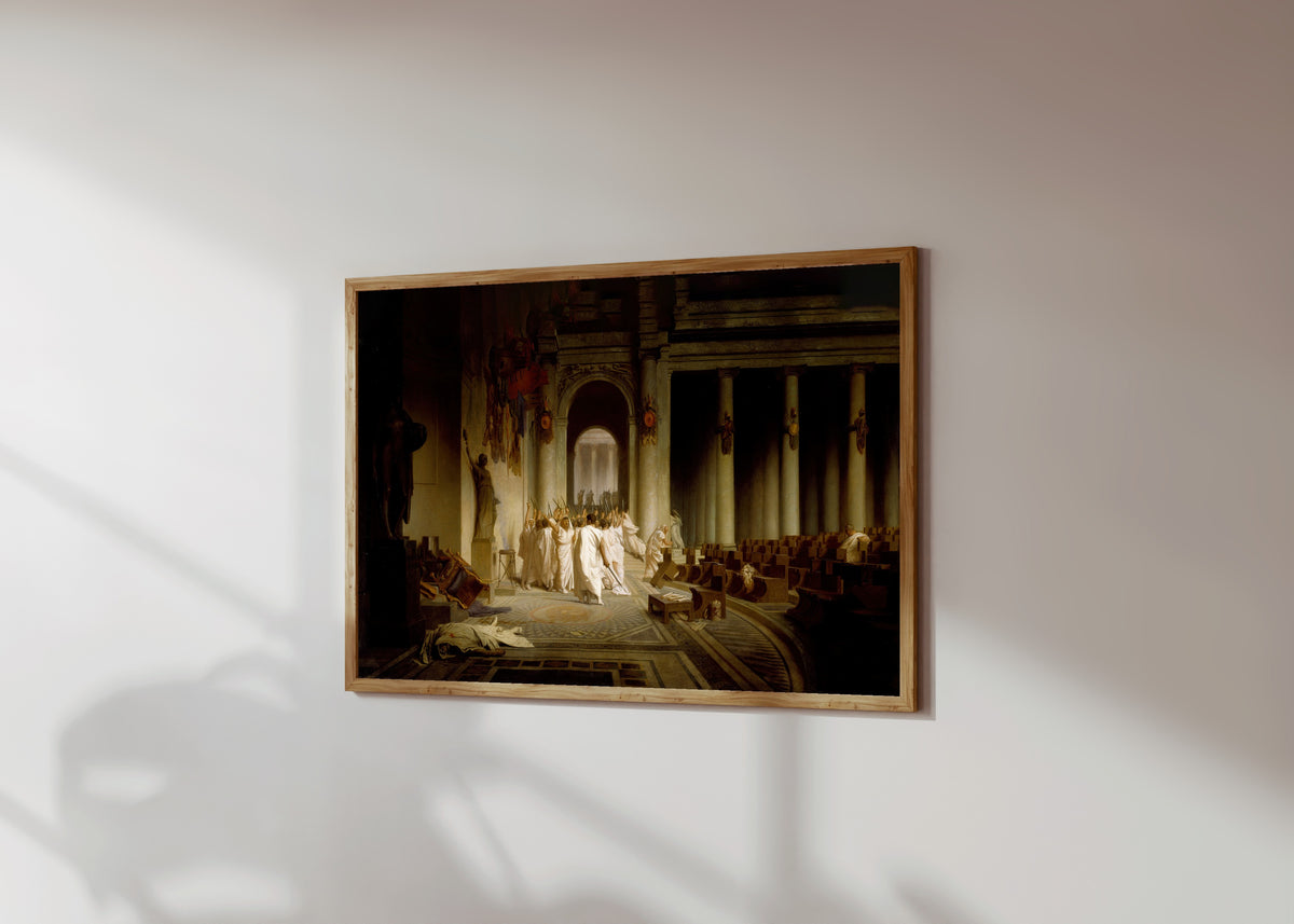 Framed art print of The Death of Caesar by Jean-Léon Gérôme, in a light wood frame on a sunlit white wall, seen at a slight angle