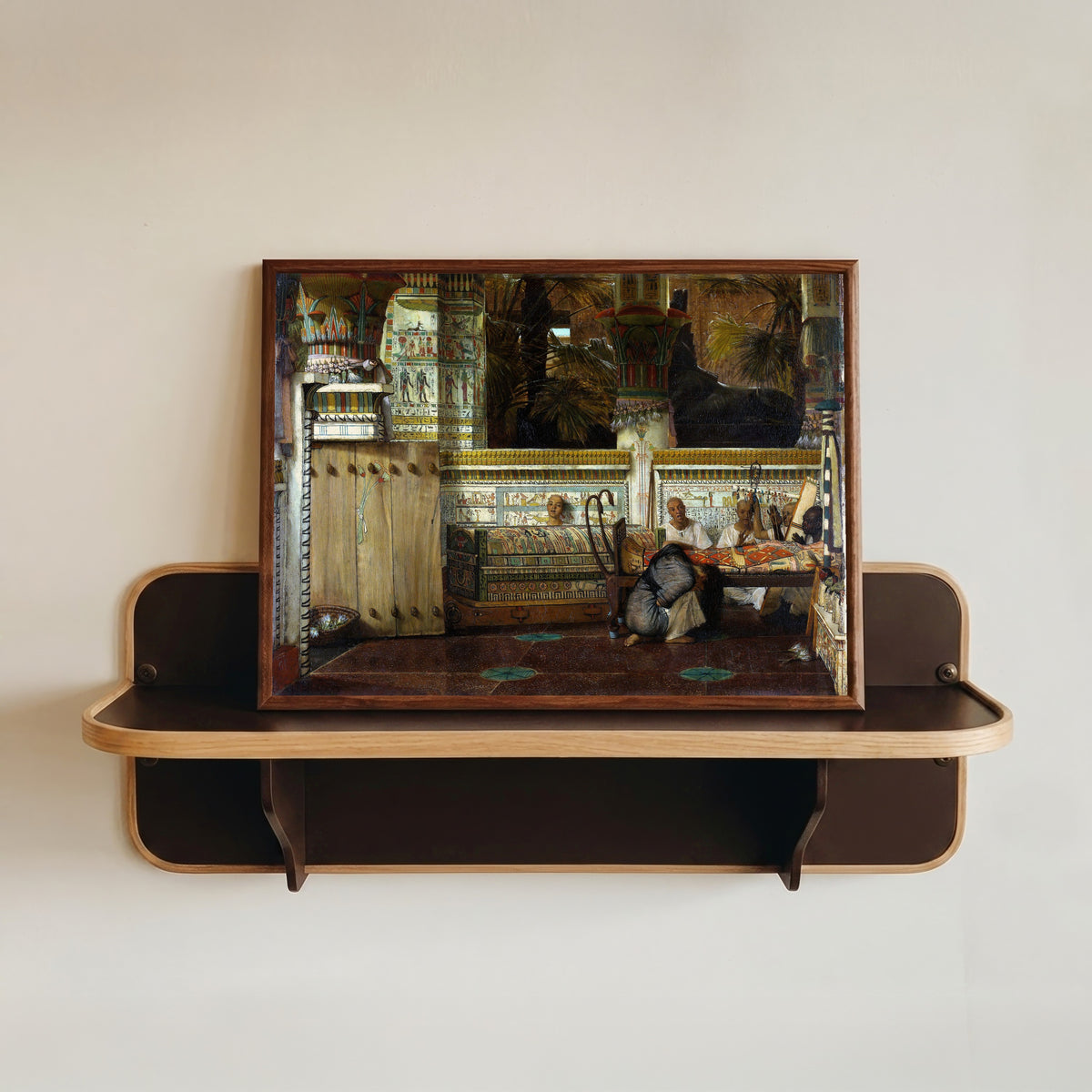 Framed art print of The Egyptian Widow by Lawrence Alma-Tadema, in a dark wood frame resting on a wall shelf