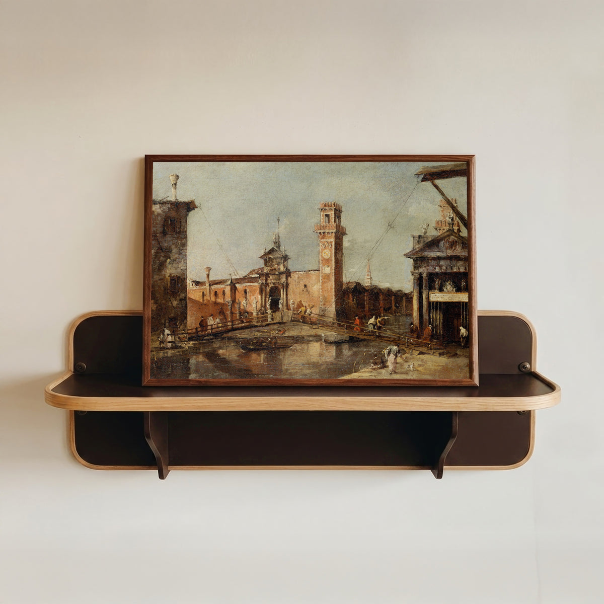 Framed art print of The Entrance to the Arsenal in Venice by Francesco Guardi, in a dark wood frame resting on a wall shelf
