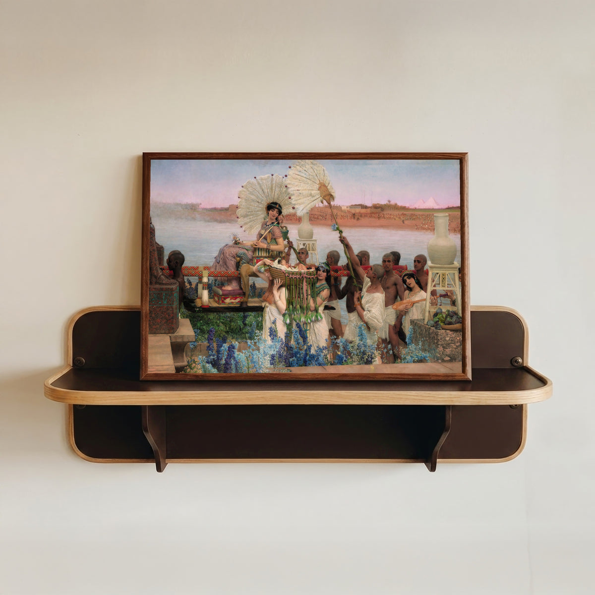 Framed art print of The Finding of Moses by Lawrence Alma-Tadema, in a dark wood frame resting on a wall shelf