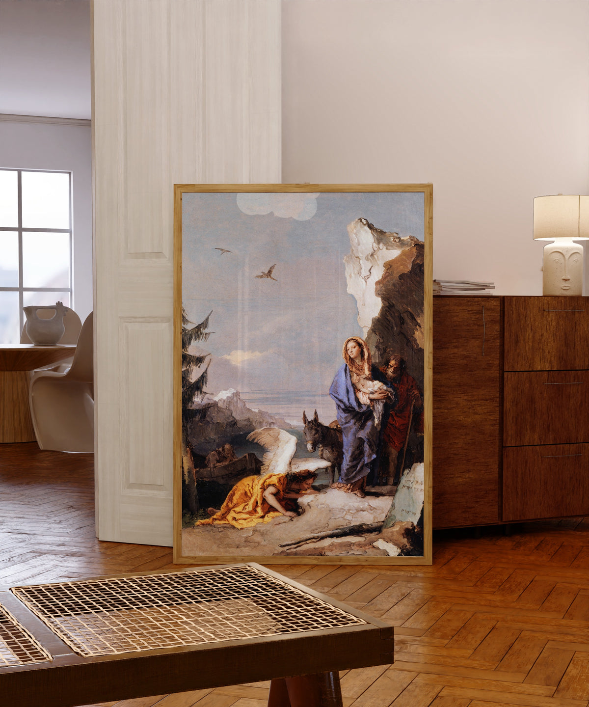 Framed art print of The Flight into Egypt by Giovanni Battista Tiepolo, in a light wood frame leaning in a warm room with a parquet floor