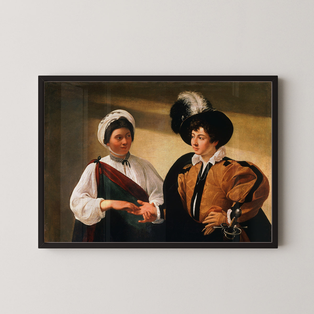 Framed art print of The Fortune Teller by Caravaggio, in a black frame on a pale wall